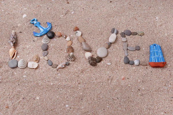 Słowo miłość wykonane z muszli i kamienie na piasku — Zdjęcie stockowe