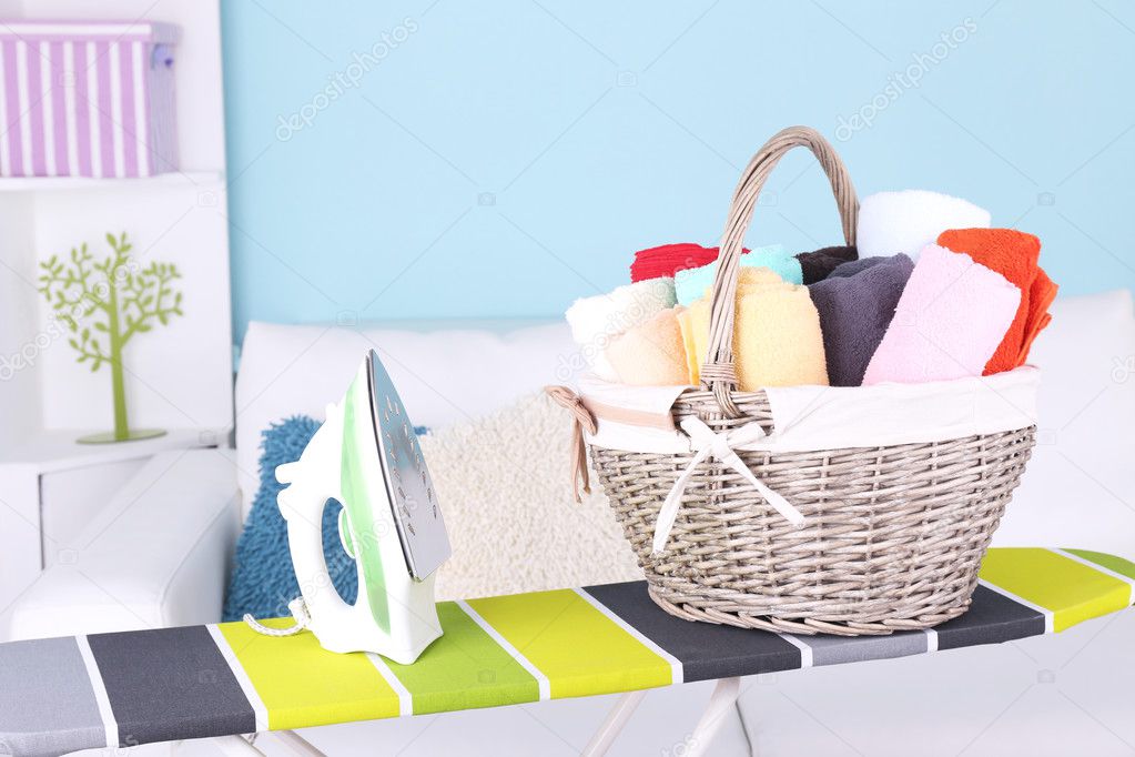 Basket with laundry and ironing board on home interior background