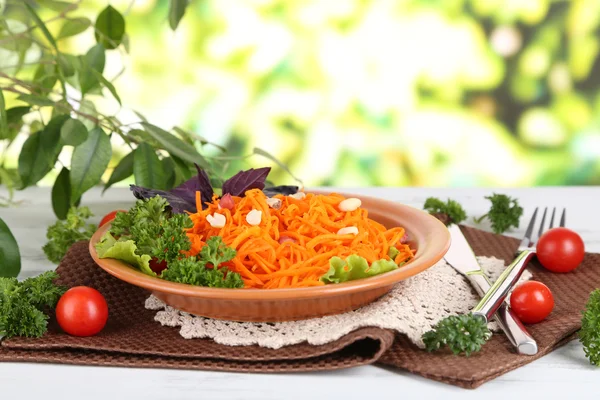 Carrot salad on plate on napkin on wooden table on nature background — Stock Photo, Image