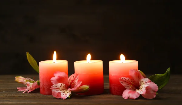 Beautiful candles with flowers on wooden table, on dark background