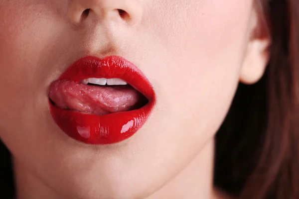 Girl licks red lips on dark background — Stock Photo, Image