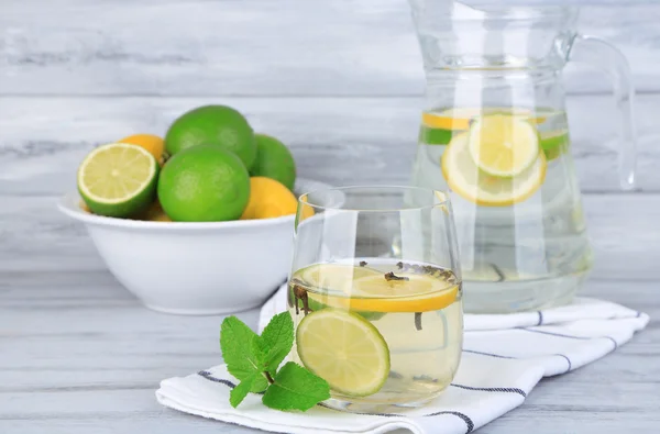 Fresh summer drink with lime and cloves in glass and jug, on color wooden background — Stock Photo, Image