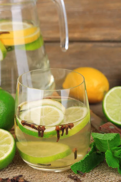 Bebida fresca de verano con cal y clavo de olor en vidrio y jarra, sobre fondo de madera de color — Foto de Stock