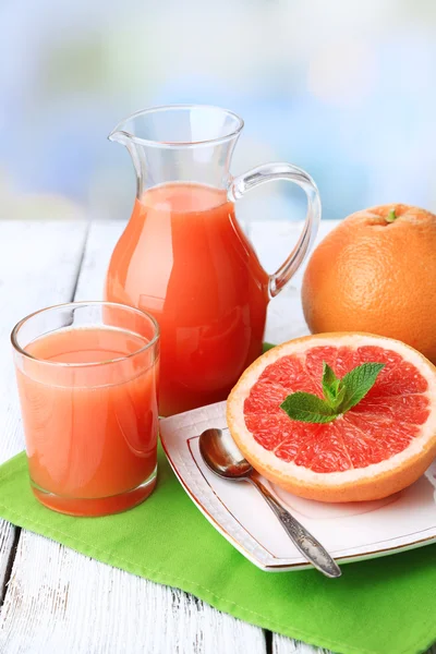 Hälfte Grapefruit, Glaskrug mit frischem Saft und Löffel auf Teller auf hellem Hintergrund — Stockfoto