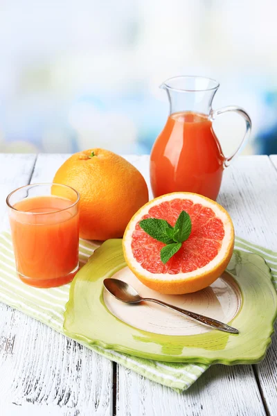 Metade de toranja, jarro de vidro com suco fresco e colher na placa no fundo claro — Fotografia de Stock