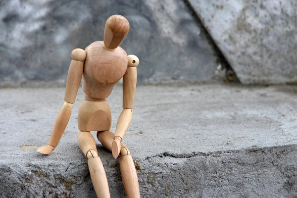 Деревянная кукла сидит на камне, на открытом воздухе — стоковое фото