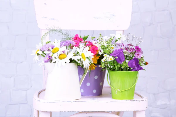 Bouquet of colorful flowers in decorative buckets, on chair, on light wall background — Stock Photo, Image