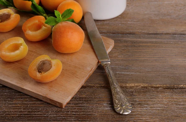 Ripe apricots with green mint leaves on cutting board, on wooden background — Stock Photo, Image