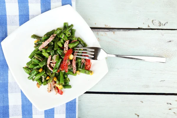 Салат с зеленой фасолью, ветчиной и кукурузой на тарелке, на фоне цвета дерева — стоковое фото