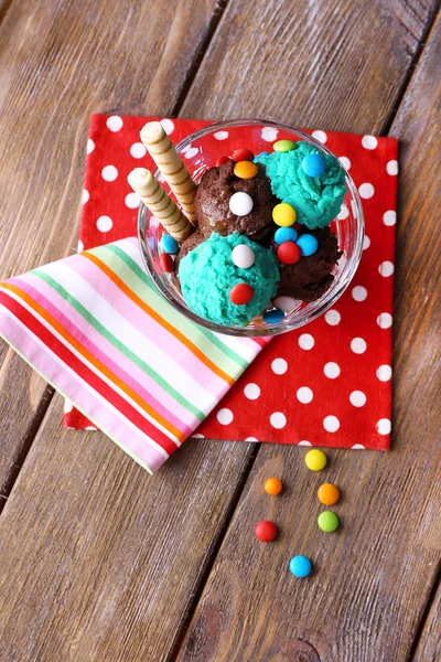Helado de chocolate con caramelos multicolores y rollos de oblea en cuenco de vidrio, sobre fondo de madera — Foto de Stock