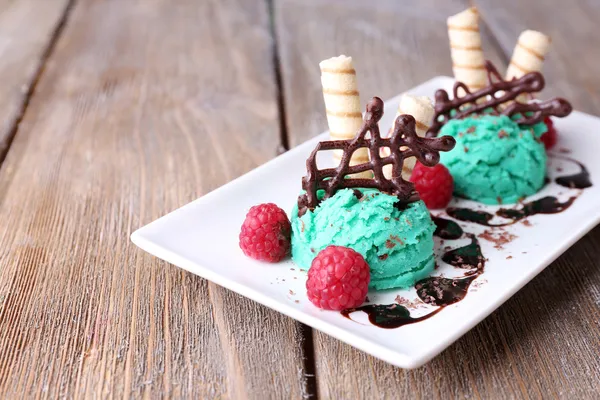 Вкусное мороженое с шоколадными украшениями и тарелкой соуса, на фоне цвета дерева — стоковое фото