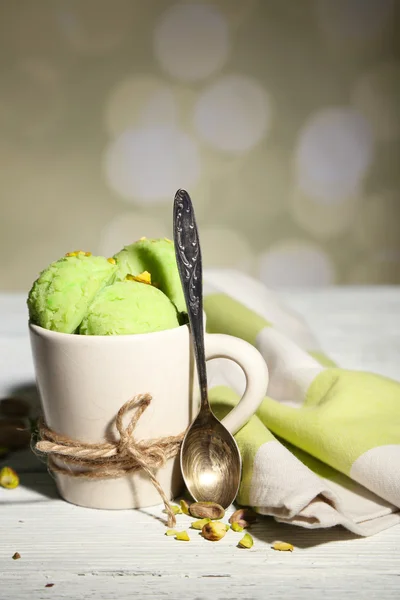 Tasty pistachio ice cream in cup on wooden table, on light background — Stock Photo, Image