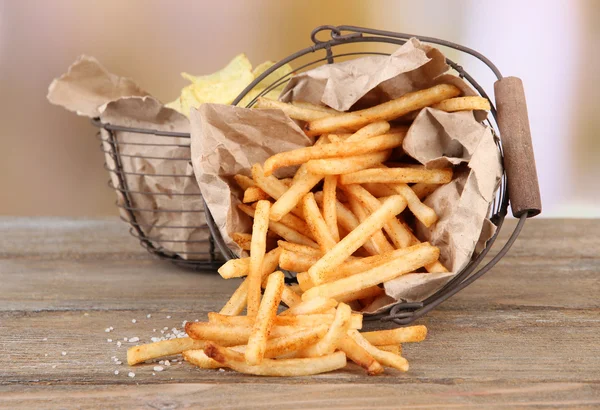 Goda pommes frites och potatischips i metall korgar på träbord, på ljus bakgrund — ストック写真