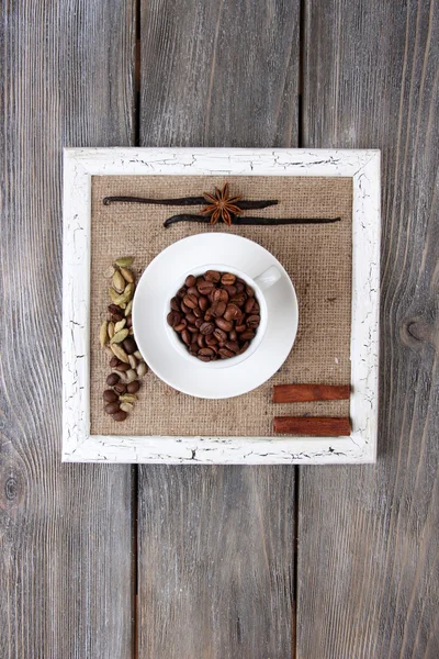 Cornice in legno con tazza bianca, chicchi di caffè e spezie su sfondo di legno — Foto Stock
