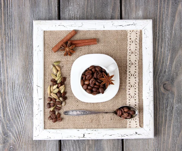 Moldura de madeira com caneca branca, grãos de café e especiarias no fundo de madeira — Fotografia de Stock
