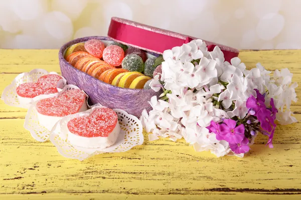 Huidige doos met snoep en bloemen op tafel op lichte achtergrond — Stockfoto