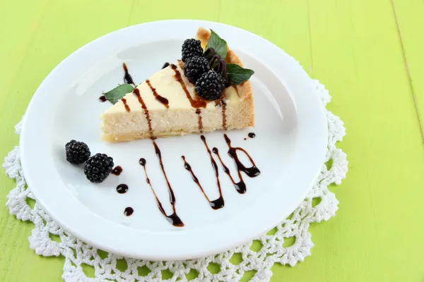 Slice of cheesecake with chocolate sauce and blackberry on plate, on wooden background — Stock Photo, Image