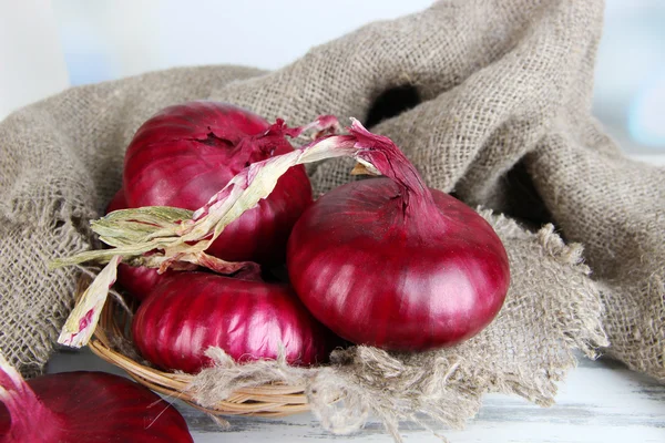 Cebollas rojas frescas en canasta de mimbre en la mesa de cerca — Foto de Stock