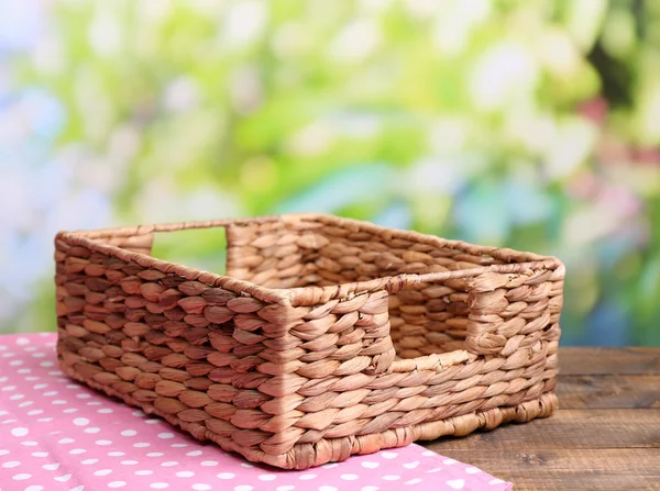 Cesta de vime vazia na mesa de madeira, no fundo brilhante — Fotografia de Stock