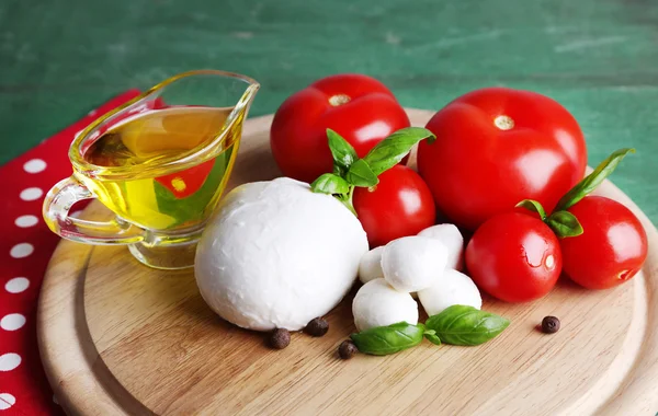 Samenstelling met smakelijke mozzarella kaas ballen, basilicum en rode tomaten, olijfolie op snijplank, op een houten achtergrond kleur — Stockfoto