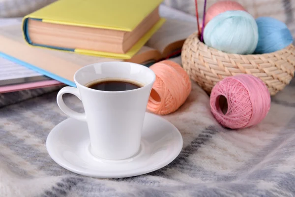 Cup of coffee and yarn for knitting on plaid with books close-up