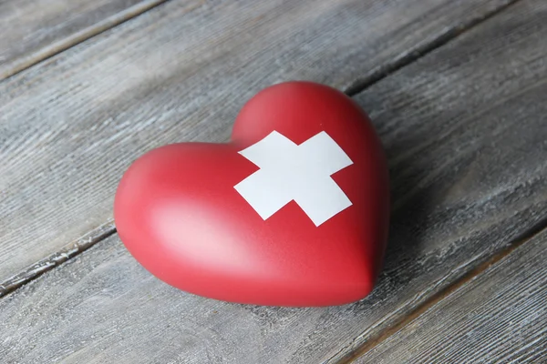 Красное сердце с крестиком на деревянном фоне — стоковое фото