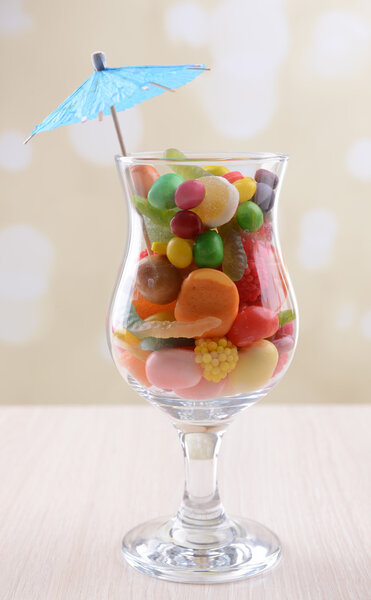 Different colorful fruit candy in glass on table on light background