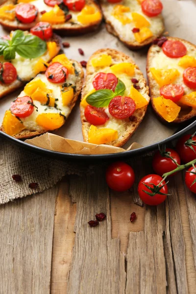 Sabroso bruschetta con tomates en la cacerola, en la mesa de madera vieja — Foto de Stock