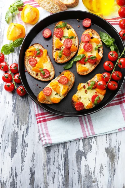 Sabroso bruschetta con tomates en la cacerola, en la mesa de madera vieja —  Fotos de Stock