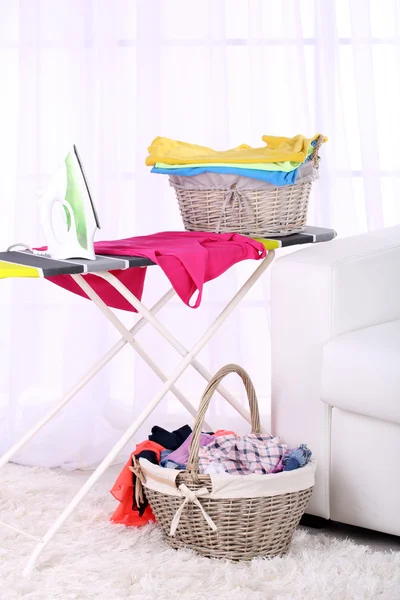 Baskets with laundry and ironing board on light home interior background — Stock Photo, Image