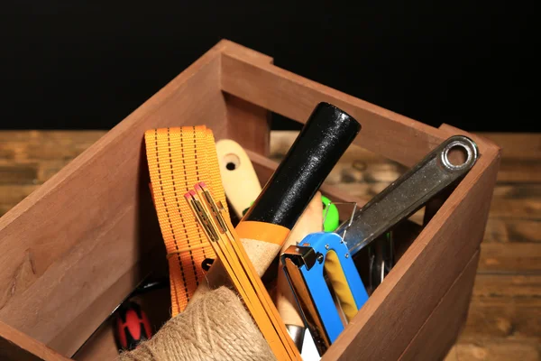 Scatola di legno con diversi utensili, su tavolo di legno, su sfondo scuro — Foto Stock