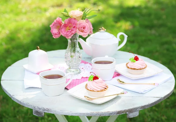 Mesa de centro con tazas de té y sabrosos pasteles en el jardín —  Fotos de Stock