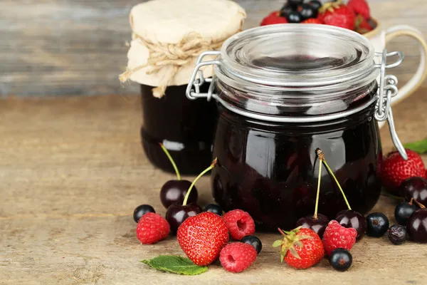 Smakelijke jam met bessen in glazen potten op houten tafel — Stockfoto