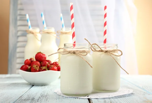 Melk in flessen met papier rietjes op tafel — Stockfoto