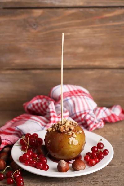 Sweet caramel apple on stick with berries, on wooden table — Stock Photo, Image