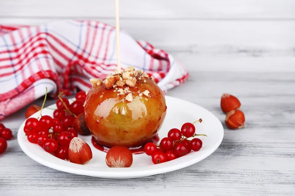 Słodkie jabłko karmelu na kij z jagód, na drewnianym stole — Zdjęcie stockowe