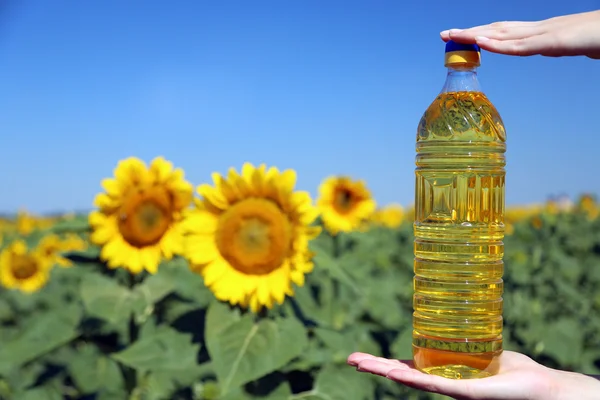 Mãos segurando garrafa com óleo no fundo do campo de girassol — Fotografia de Stock