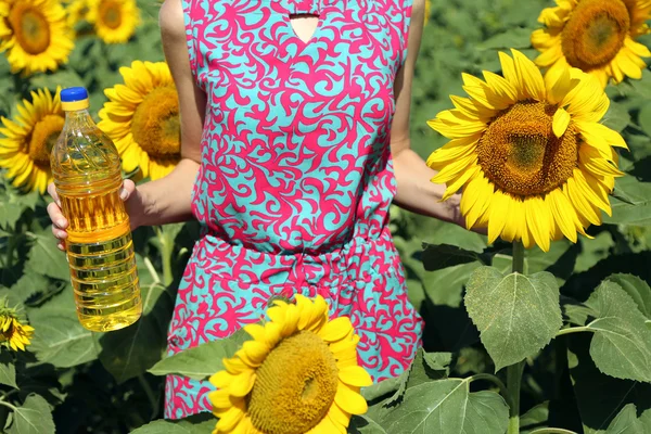 Jonge vrouw met fles van olie en zonnebloem in veld — Stockfoto