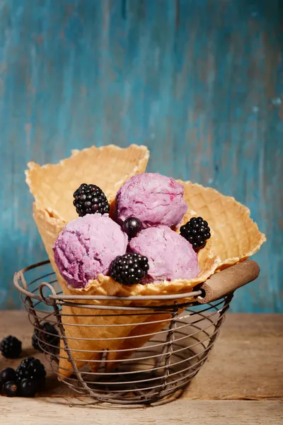 Вкусное мороженое с ягодами в вафельном конусе на синем деревянном фоне — стоковое фото