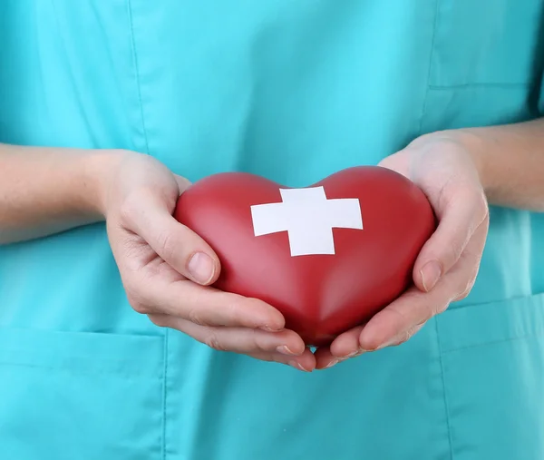 Красное сердце с поперечным знаком в руке врача, крупным планом, изолированное на белом — стоковое фото