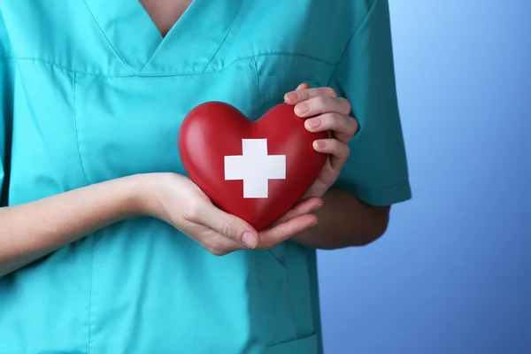 Rotes Herz mit Kreuzzeichen in der Hand des Arztes, Nahaufnahme, auf Farbhintergrund — Stockfoto