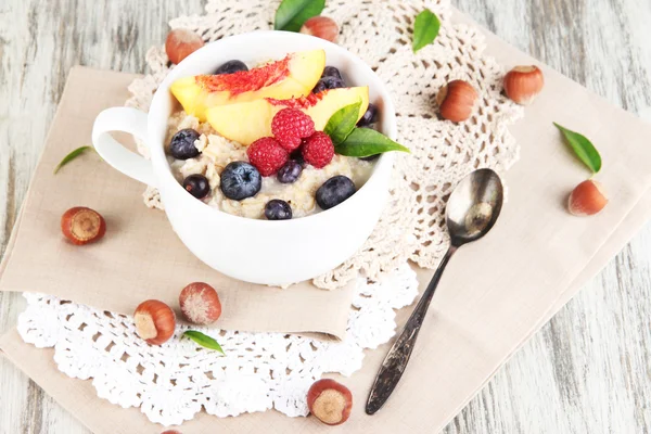 Oatmeal in cup with berries on napkins on wooden table — Stock Photo, Image