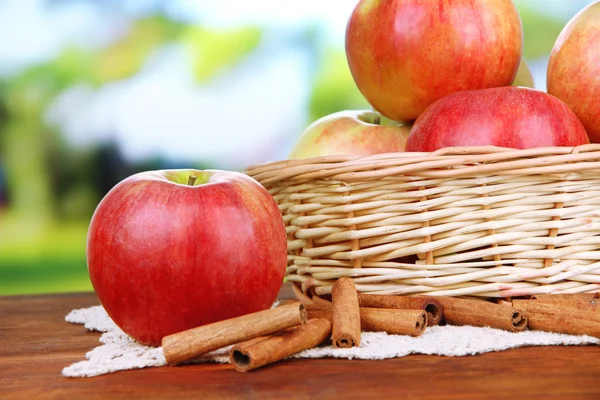 Ripe apples with with cinnamon sticks  on  wooden table, on bright background — Stock Photo, Image