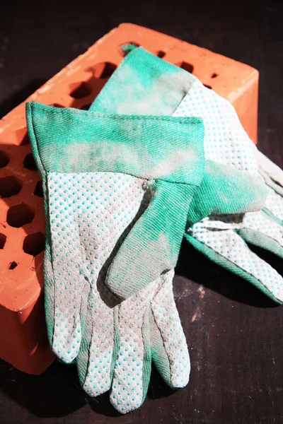 Dirty used fabric gloves and bricks on wooden background — Stock Photo, Image