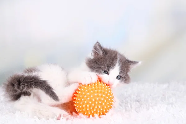 Gatinho bonito brincando com bola no tapete branco, no fundo claro — Fotografia de Stock