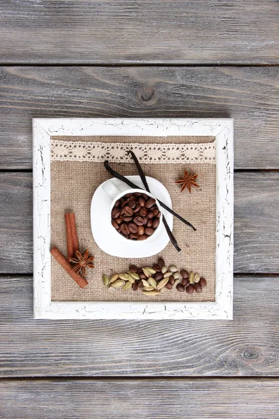 Wooden frame with white mug, coffee grains and spices on wooden background — Stock Photo, Image