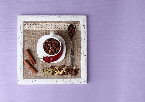 Wooden frame with white mug, coffee grains and spices on color background — Stock Photo, Image