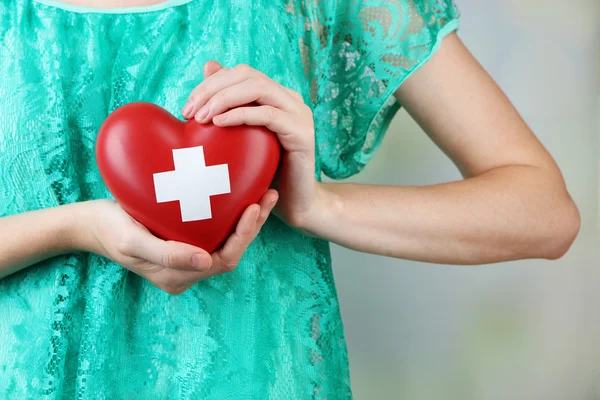 Red heart with cross sign in female hands — Stock Photo, Image
