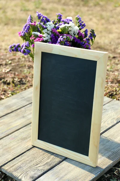 Hermosas flores silvestres en jarrón y marco vacío en mesa de madera sobre fondo de campo —  Fotos de Stock