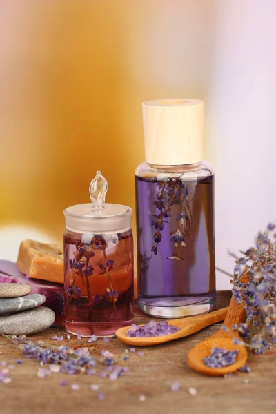 Спа-натюрморт с лавандовым маслом и цветами на деревянном столе, на светлом фоне — стоковое фото